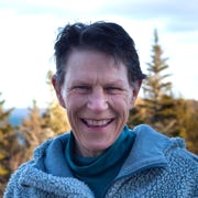 Robin Mann smiling, outdoors with a blue sky and treetops behind her. 