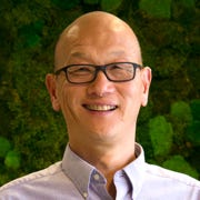 Dan Chu, smiling in front of a wall of green plants. 